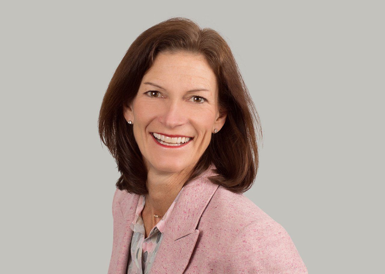 Woman in pink blazer smiling at the camera against a gray background.