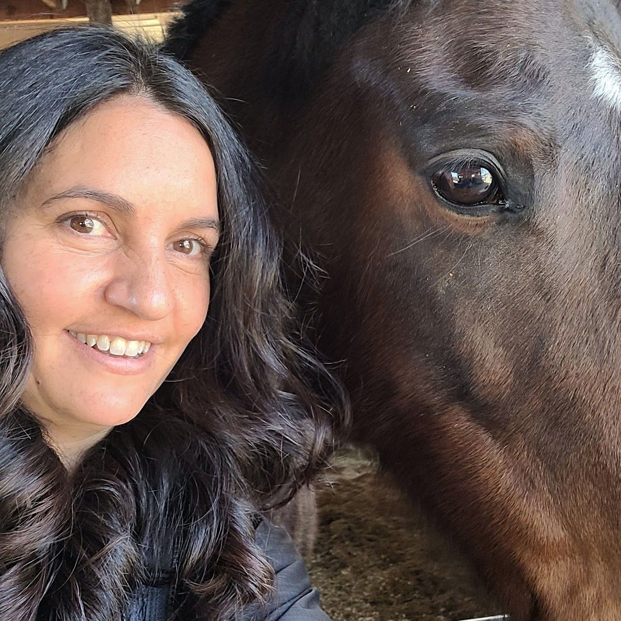 Woman smiling with dark hair, beside a brown horse with a white marking on its face.