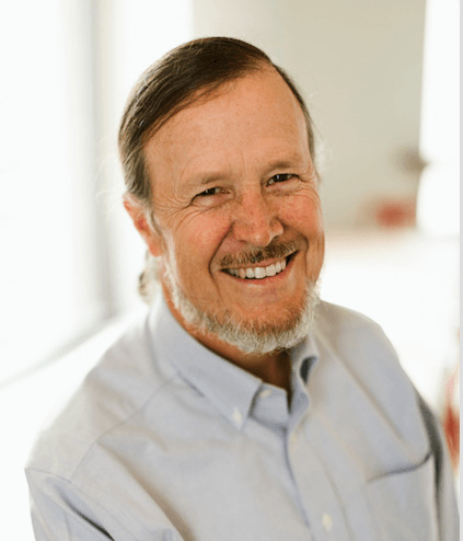 Smiling man with beard, light blue shirt, in a well-lit indoor setting.