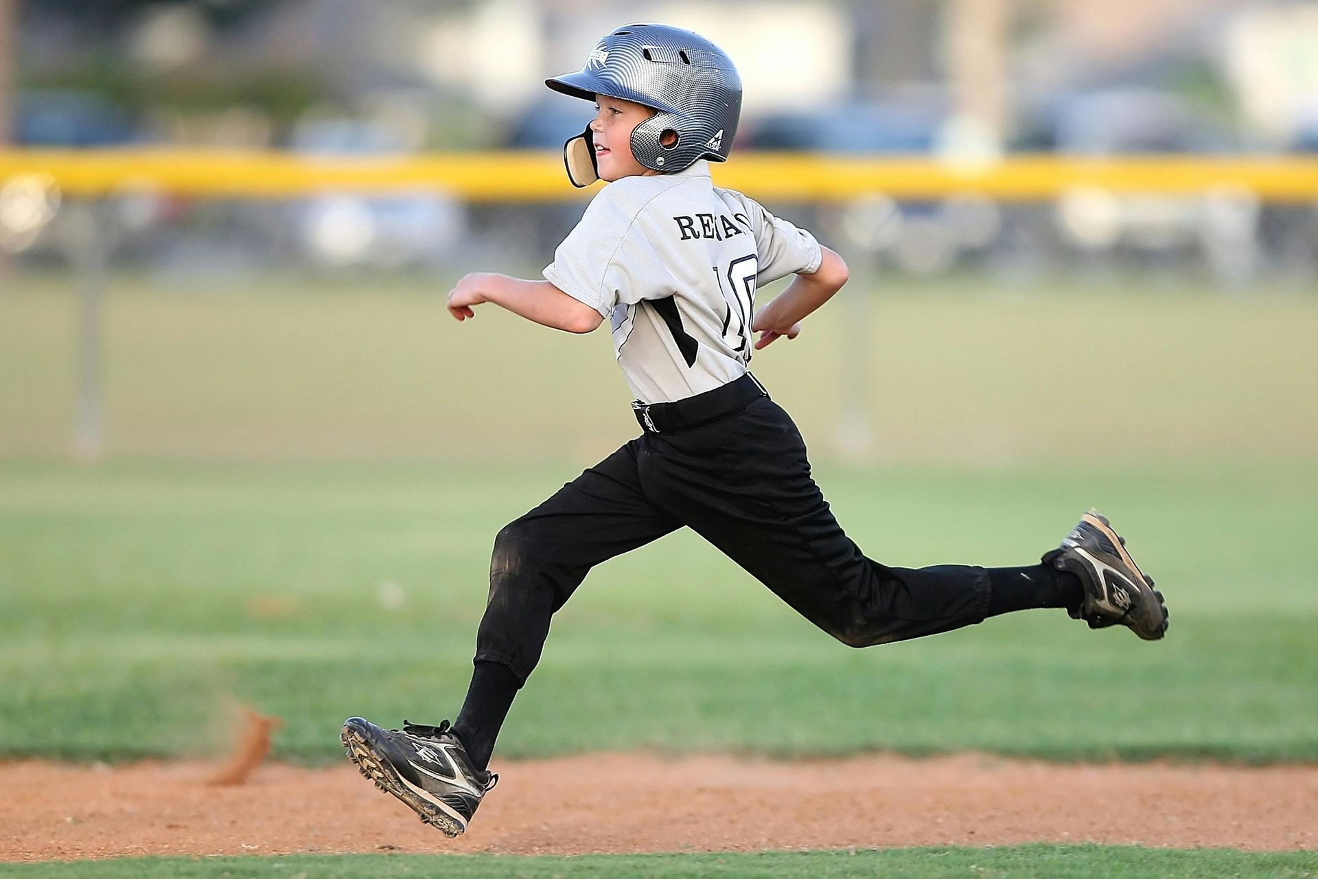 Youth baseball player running, wearing helmet and uniform, on a baseball field.