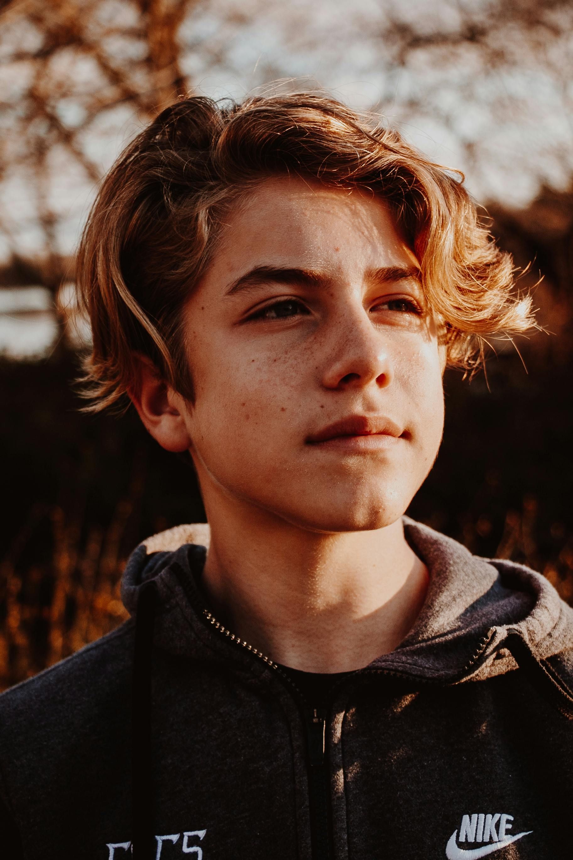 Young person with light brown hair, looking to the side, wearing a dark gray hooded sweatshirt.