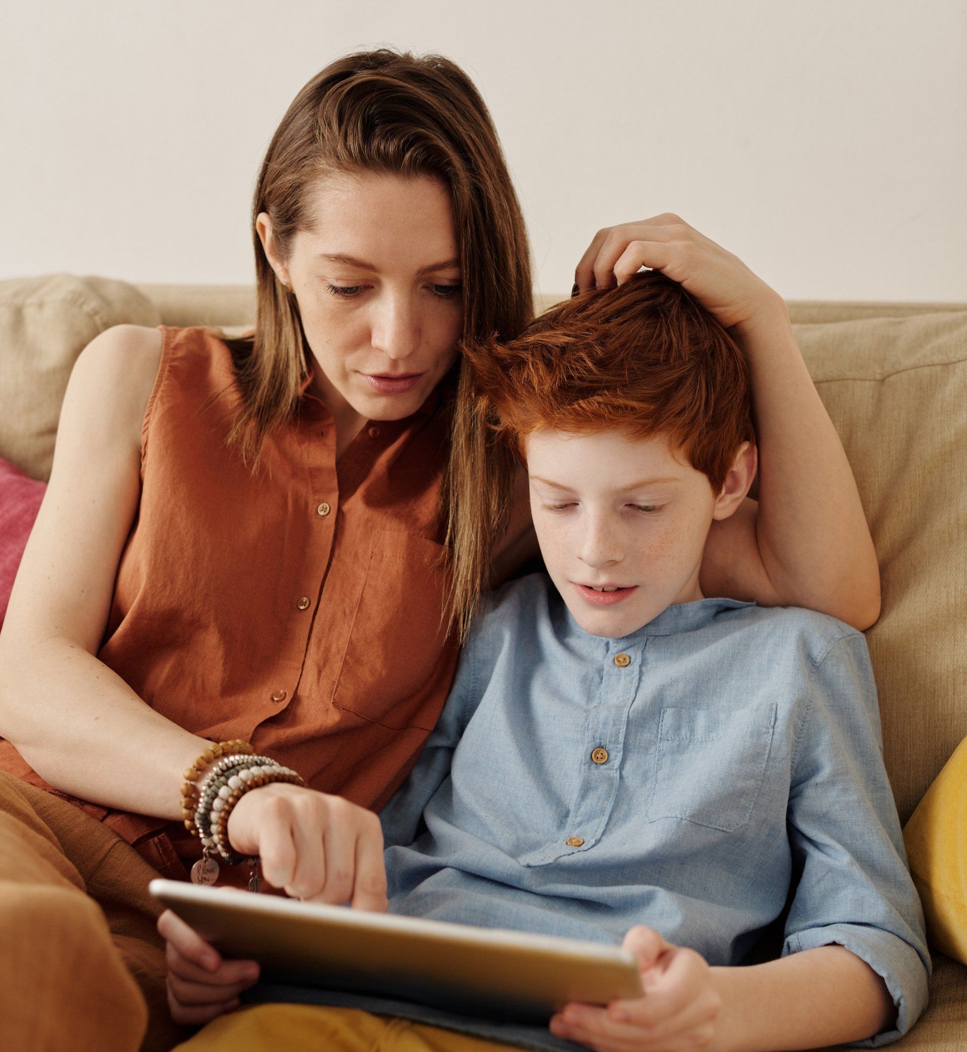 Woman and child looking at a tablet together while sitting on a couch.