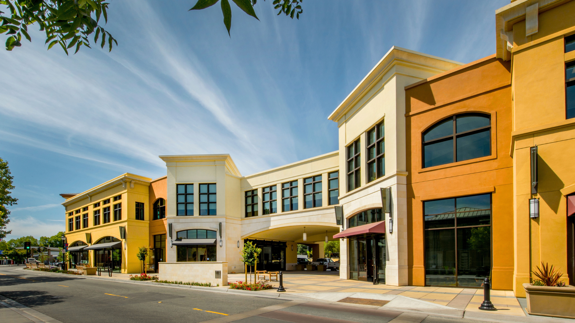 Sunny street view of modern storefronts with yellow, cream, and orange facades under a blue sky