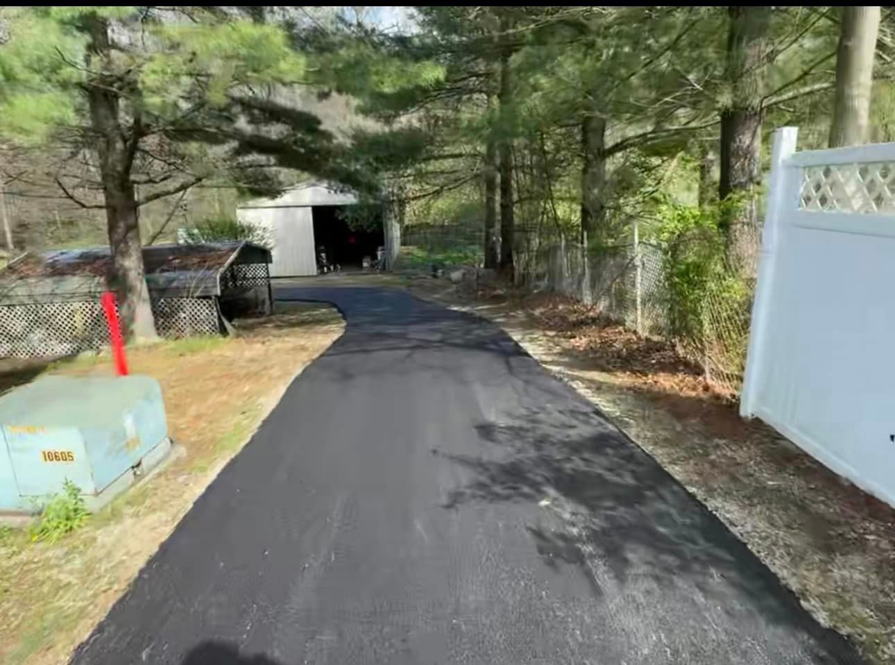 A black asphalt driveway leading to a garage and a white fence.
