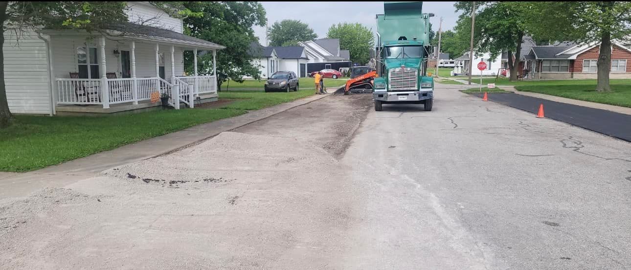 A truck is driving down a street next to a house.