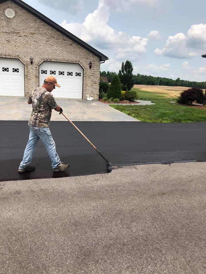 A man is painting a driveway in front of a house.