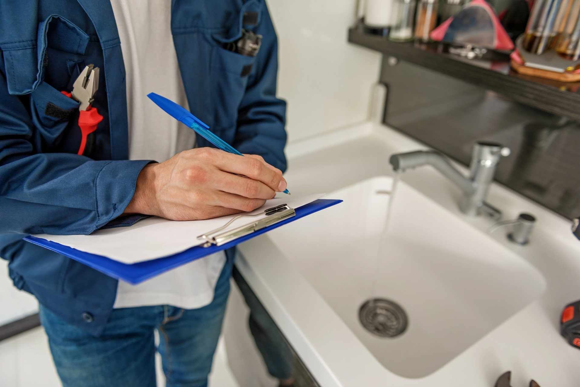 Person writing on a clipboard beside a white bathroom sink with chrome faucet