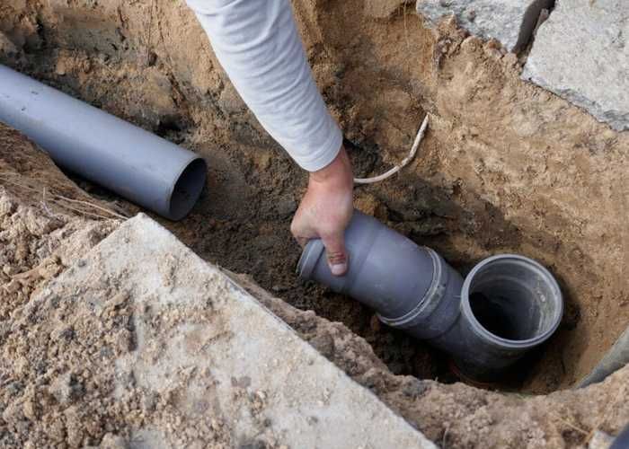 Worker connecting gray PVC pipes in a trench during plumbing installation