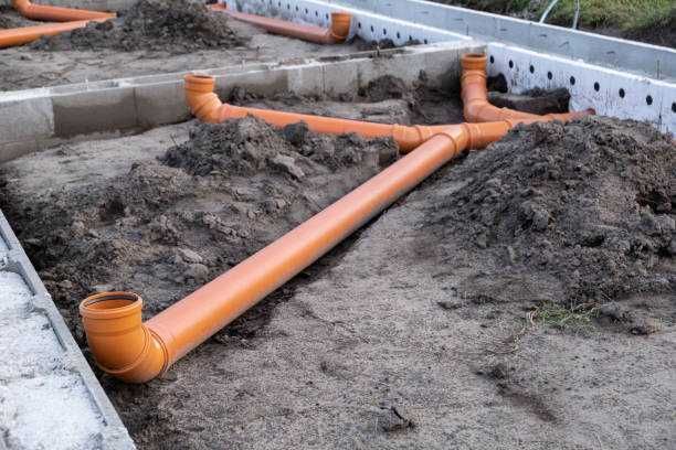 Orange PVC pipes laid in dirt trenches at a construction site