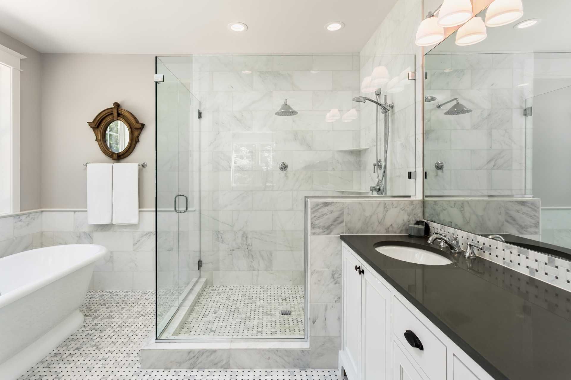 Bright modern bathroom with glass shower, freestanding tub, vanity, and marble tile.