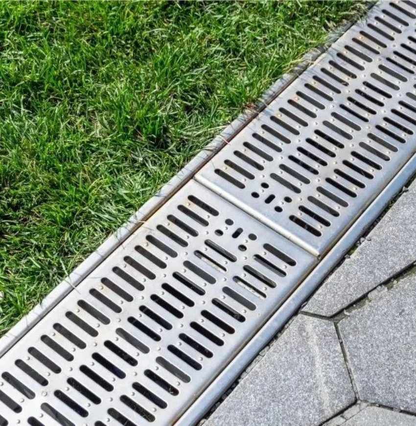 Metal drainage grate beside green grass and gray paving stones