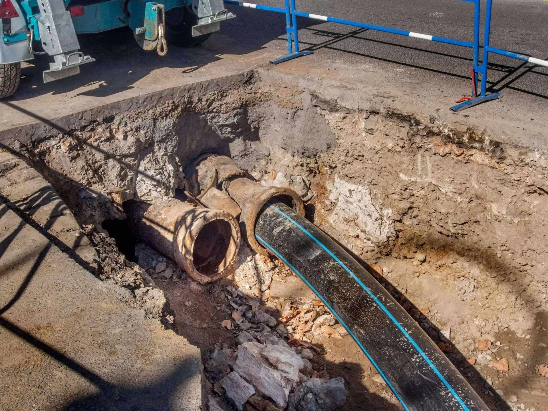 Excavation site with a large broken pipe and exposed utility lines in a dirt trench