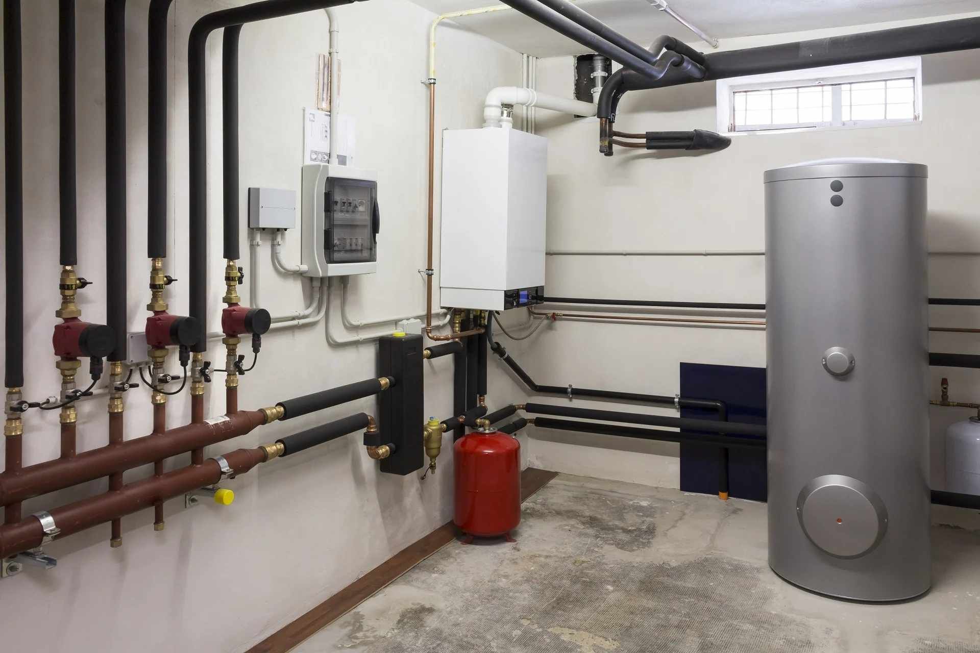 Boiler room with pipes, water heater, and utility equipment against white walls and concrete floor