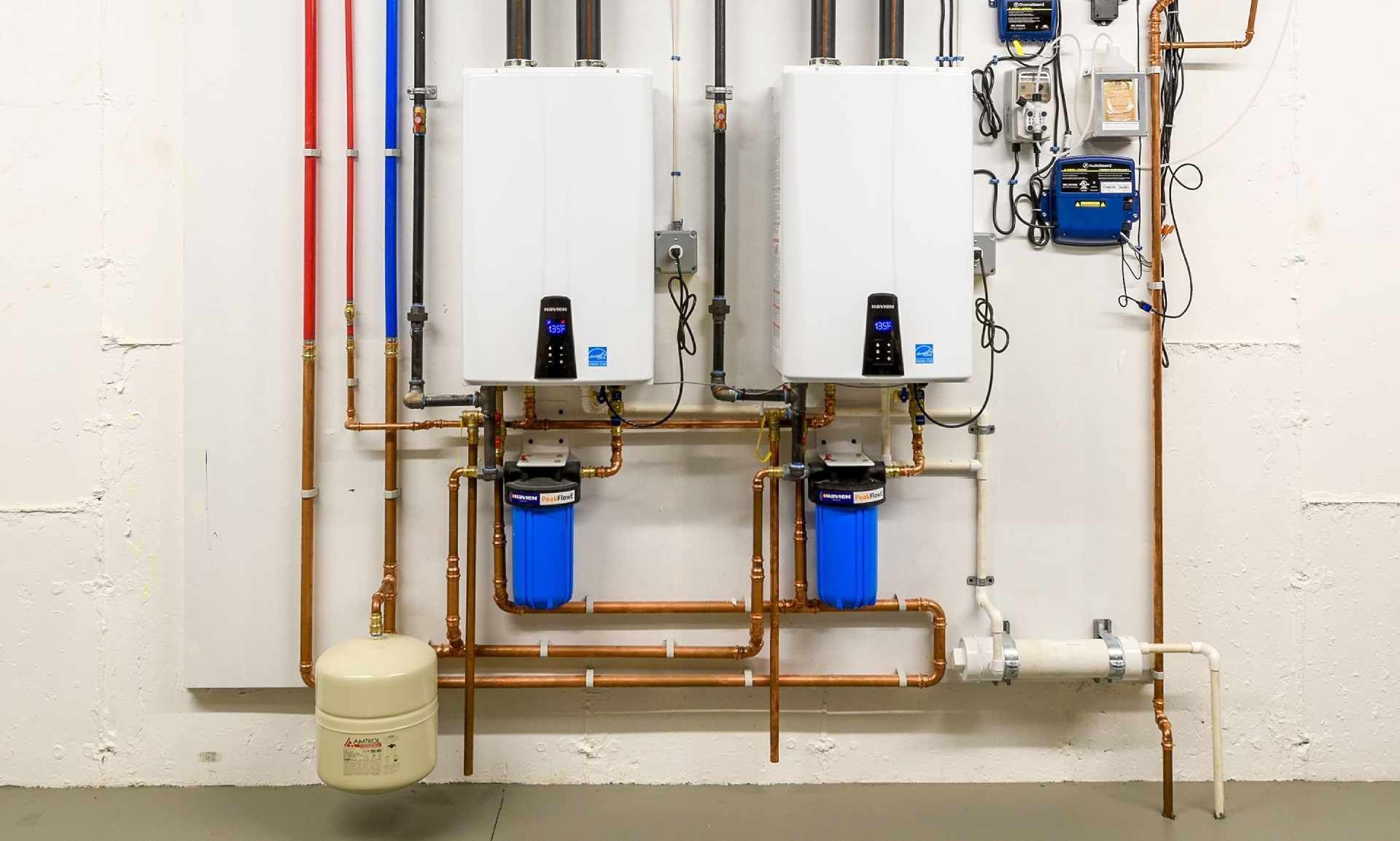 Two white wall-mounted water heaters with copper pipes and blue filter canisters in a utility room