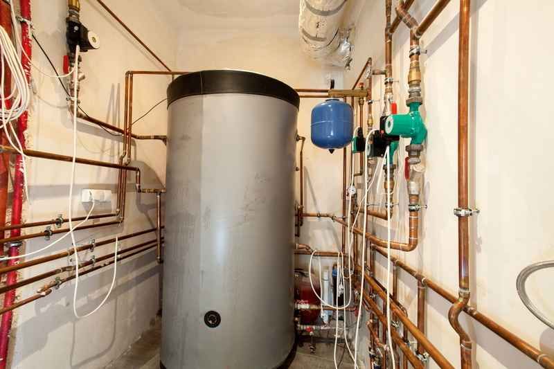 Utility room with a large gray water heater, copper pipes, and valves along white walls