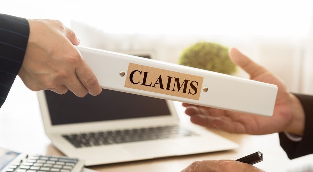 A Person is Handing a Binder With the Word Claims on It — Paton Hooke Lawyers & Conveyancers In Taree, NSW