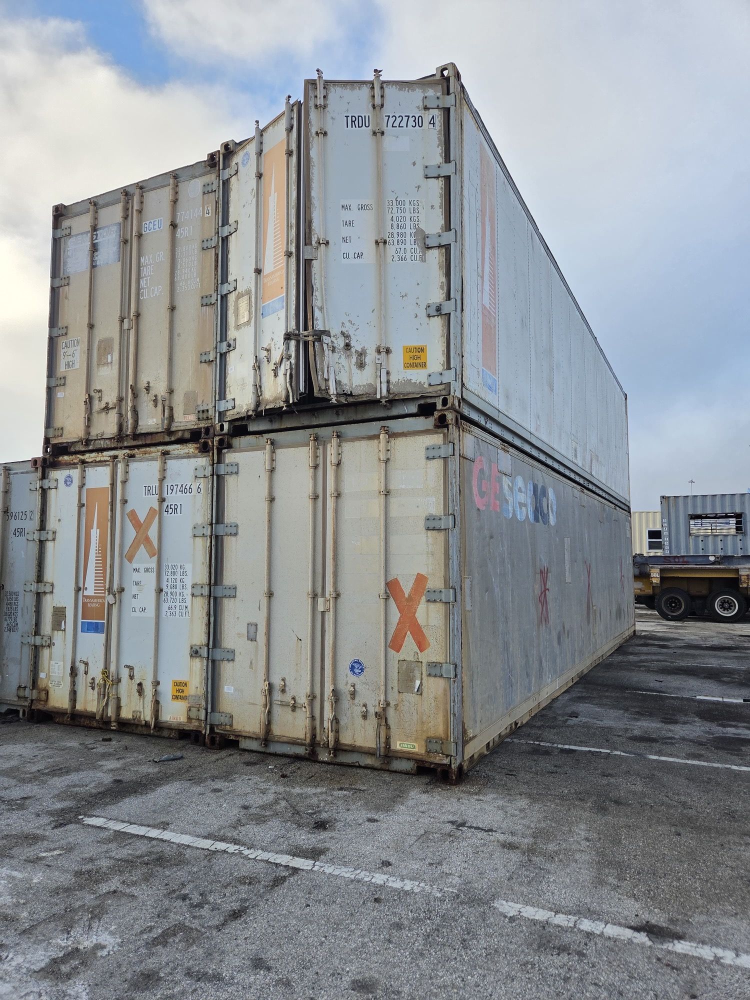 Stack of weathered shipping containers in an outdoor lot on a cloudy day.
