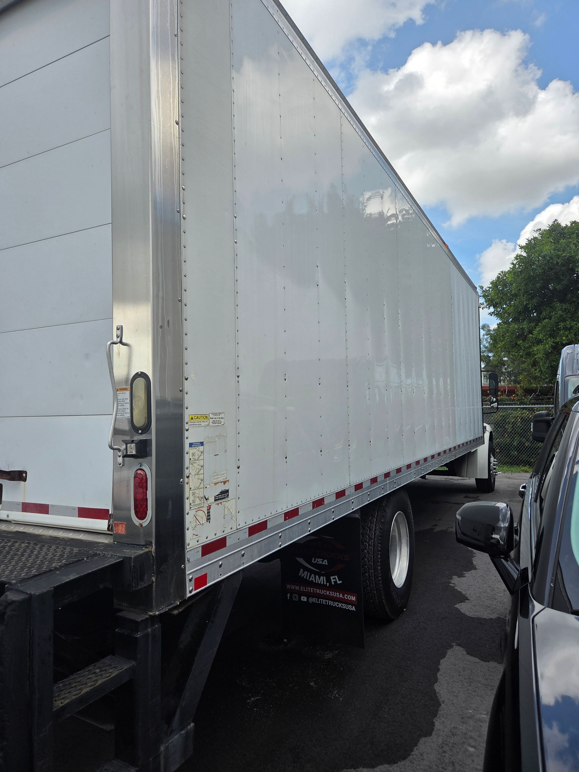 White box truck, rear view, parked outdoors, under a partly cloudy sky.