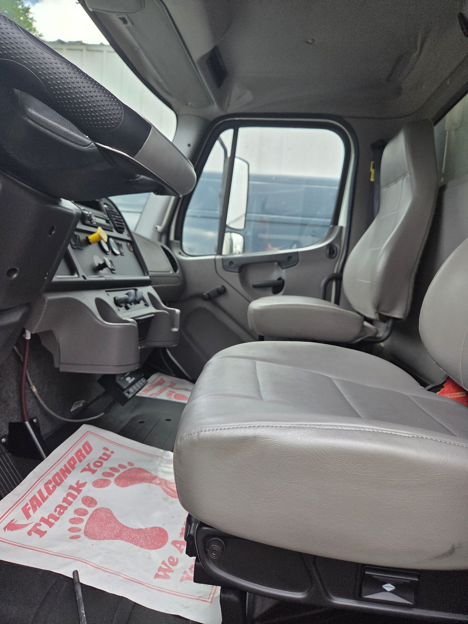 Interior view of a truck cab, with driver's seat, steering wheel, dashboard, and a foot-shaped floor mat.