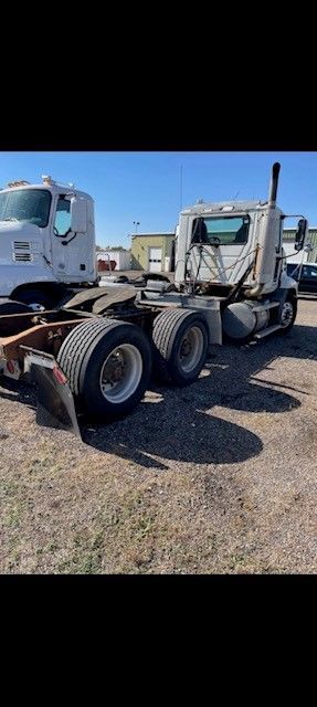 Semi-truck parked on a gravel lot under a blue sky, facing right.