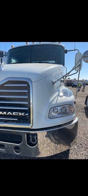 White Mack truck with chrome details, parked outdoors on a sunny day.