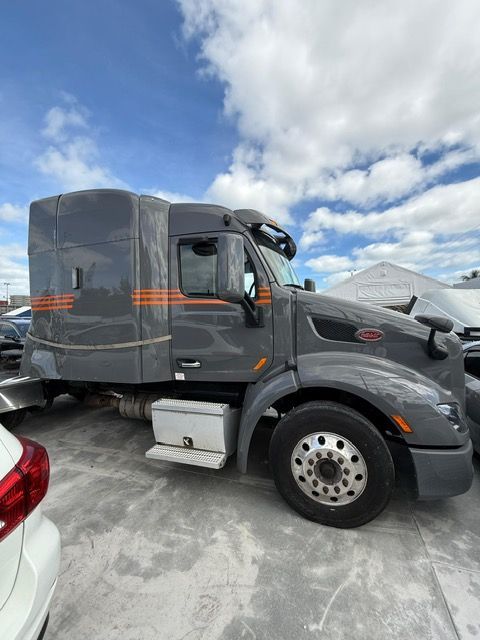 Gray Peterbilt semi-truck parked outdoors under a cloudy sky. Orange stripes on the sleeper cab.