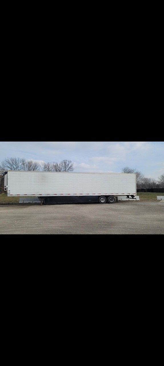 White semi-trailer parked outdoors on a gravel lot; trees in the background, overcast sky.
