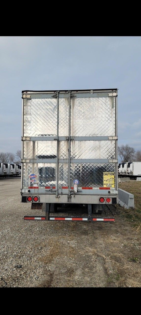 Rear view of a silver semi-trailer with red and white reflective stripes, parked outdoors.