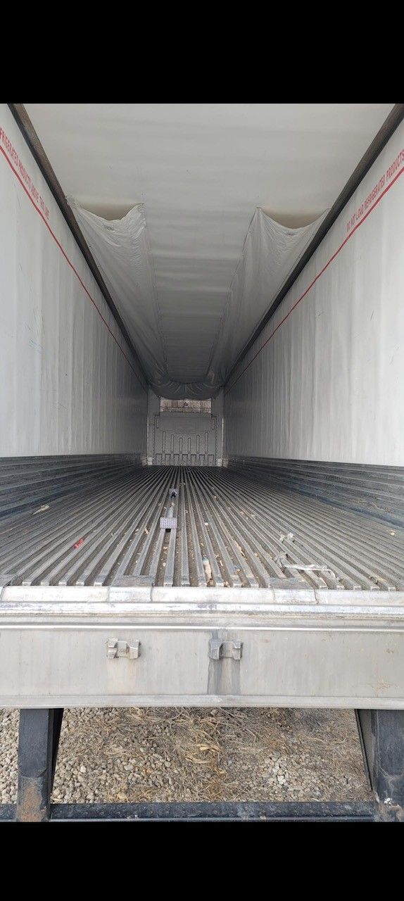 Interior of an empty refrigerated semi-trailer, showing the grated floor and insulated walls.