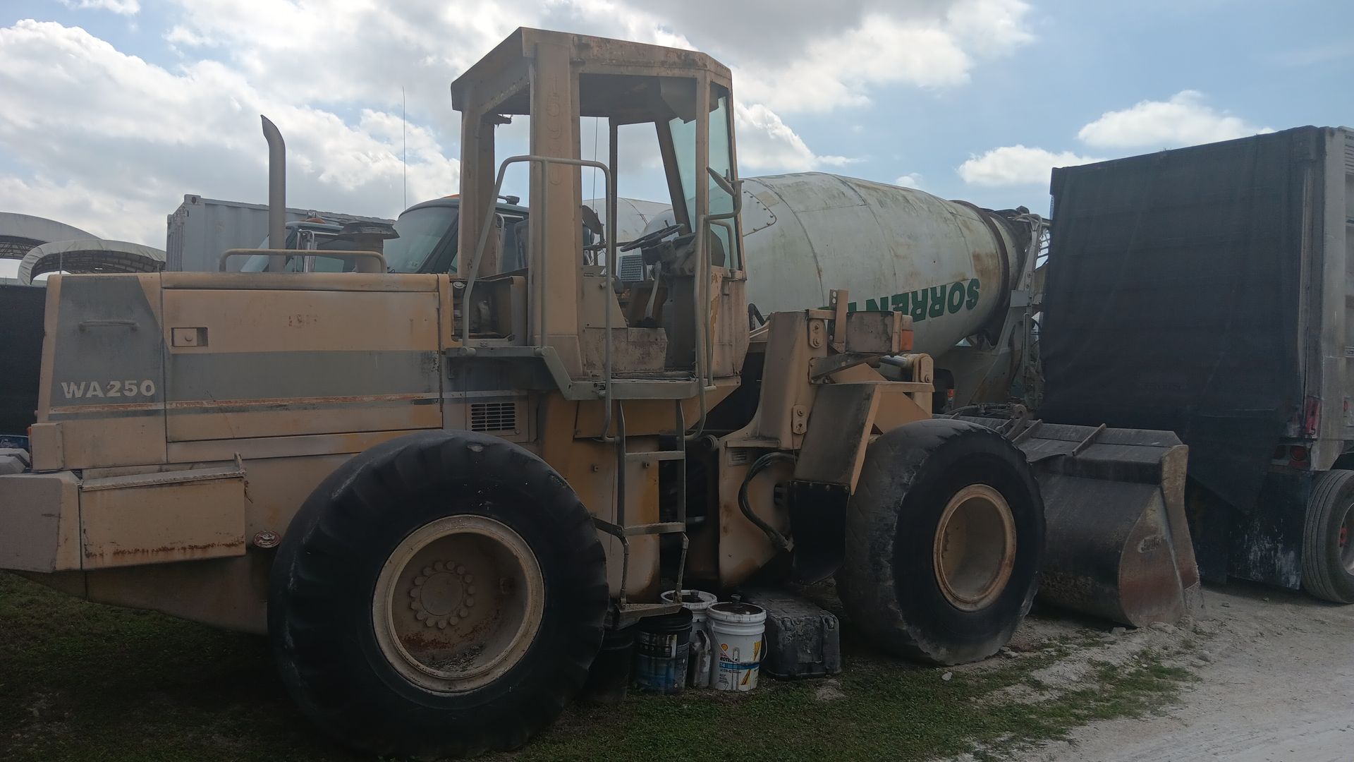 Yellow loader next to a cement mixer and a truck on a sunny day.