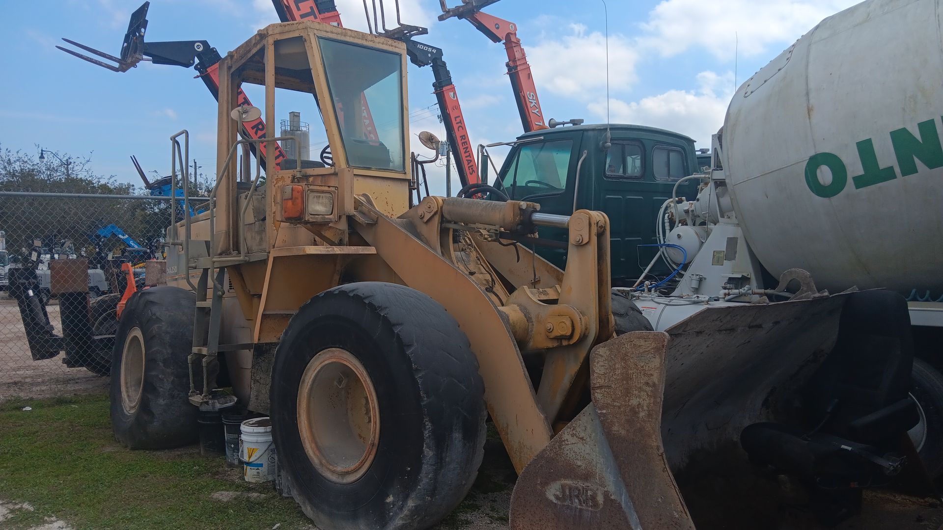 Yellow loader with large tires, next to a cement truck and a dark green vehicle.