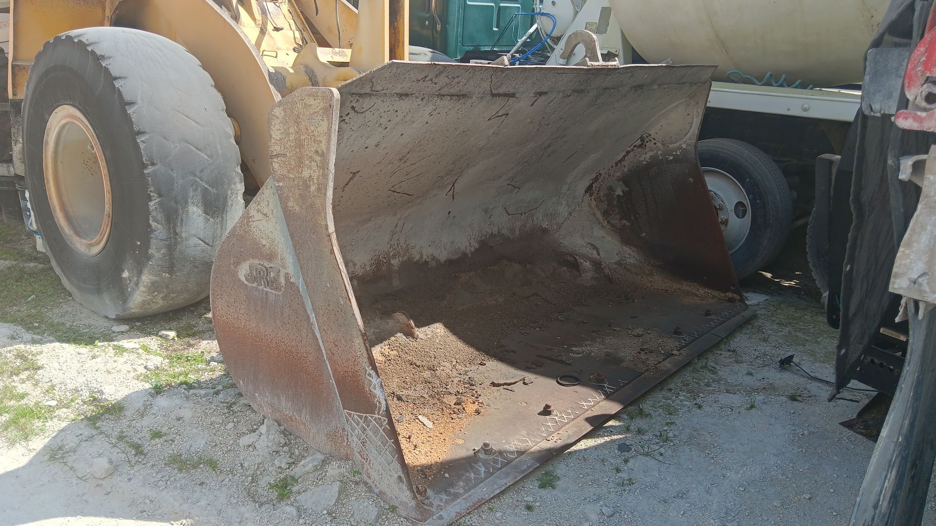 Rust-colored front-end loader bucket, part of heavy machinery, outdoors on a sunny day.