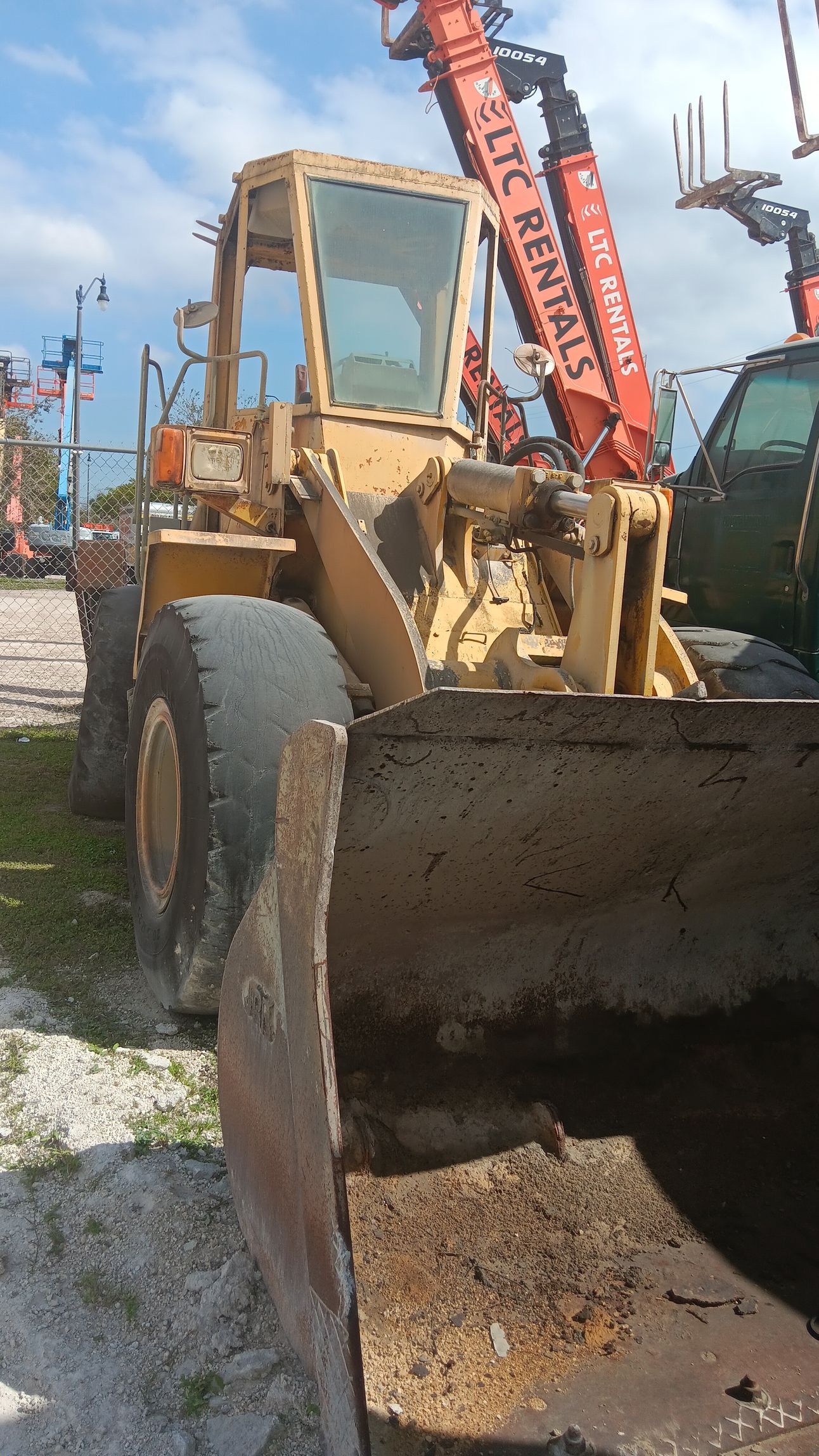 Yellow front-end loader with raised bucket; parked outdoors near other machinery.
