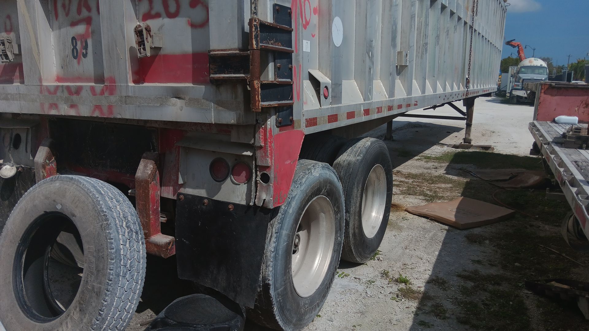 Back of a large silver semi-trailer with red accents; a spare tire leans against it.