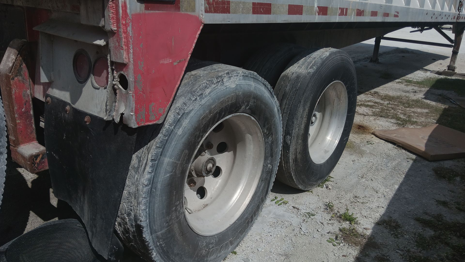 Truck trailer's rear tires, dusty, close up view; red, white, gray, and black colors; outdoors.