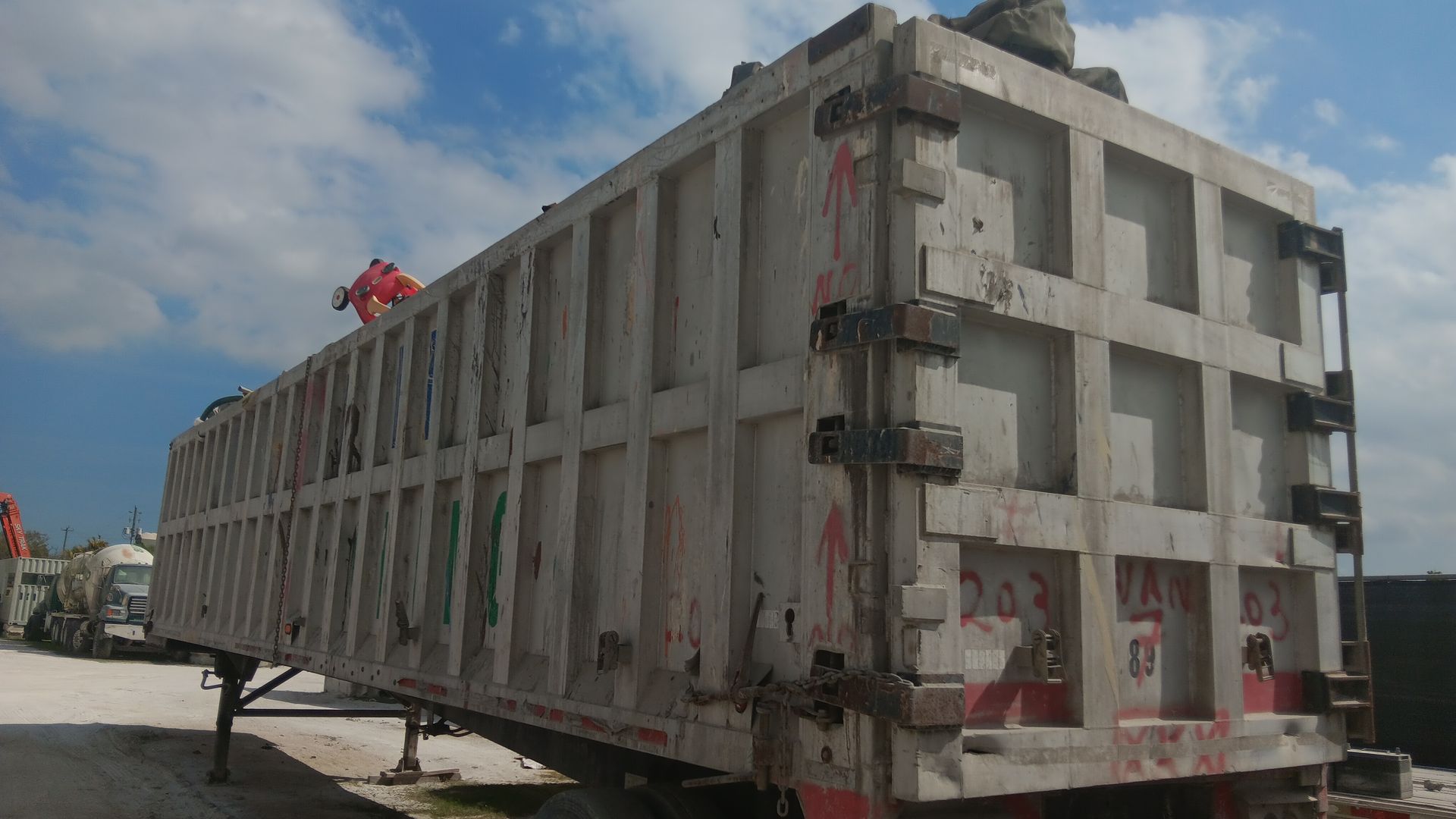 Large, weathered dump trailer in a yard, under a partly cloudy sky.