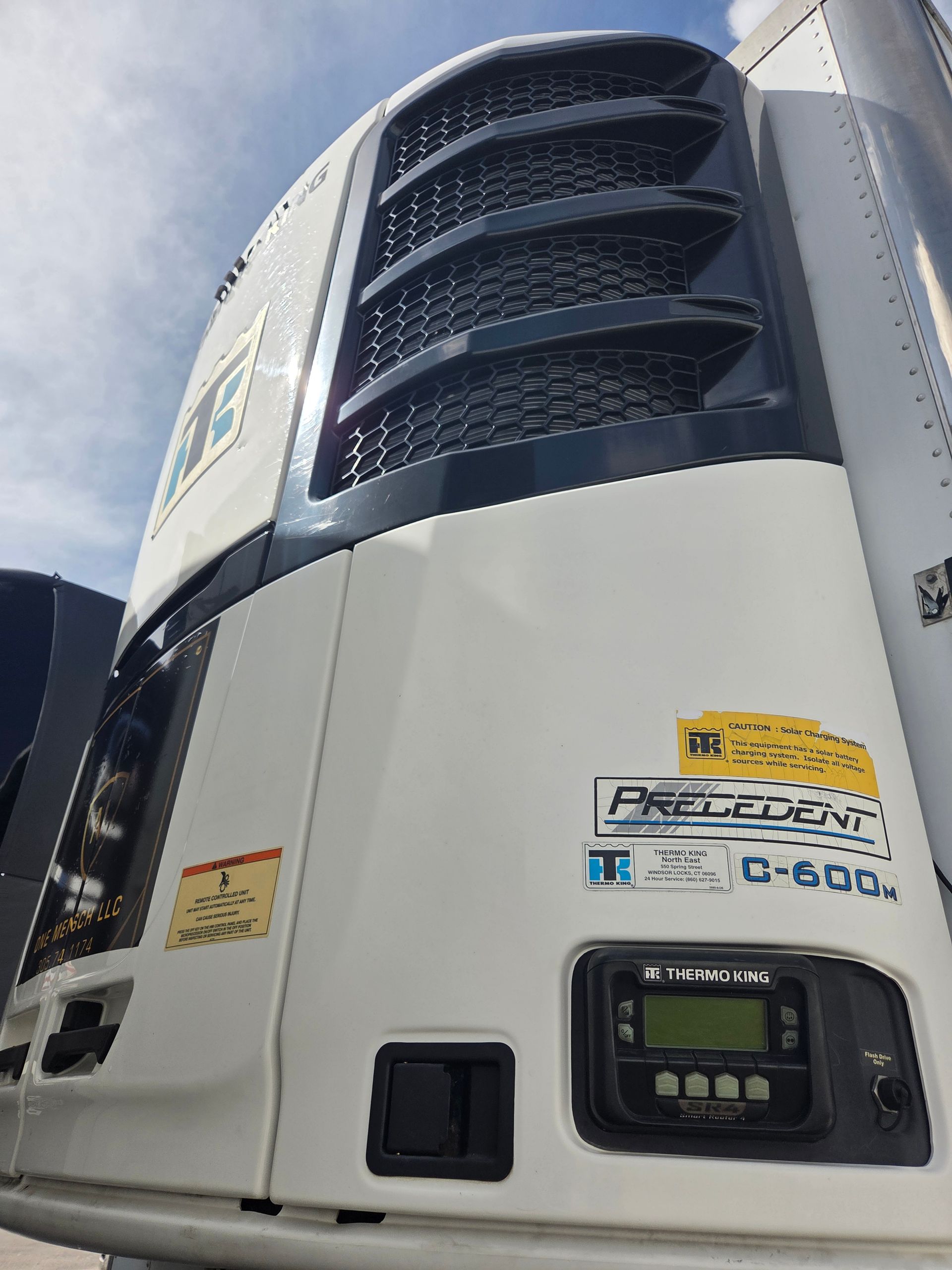 White refrigeration unit on a truck, with a black top. Blue sky in the background.