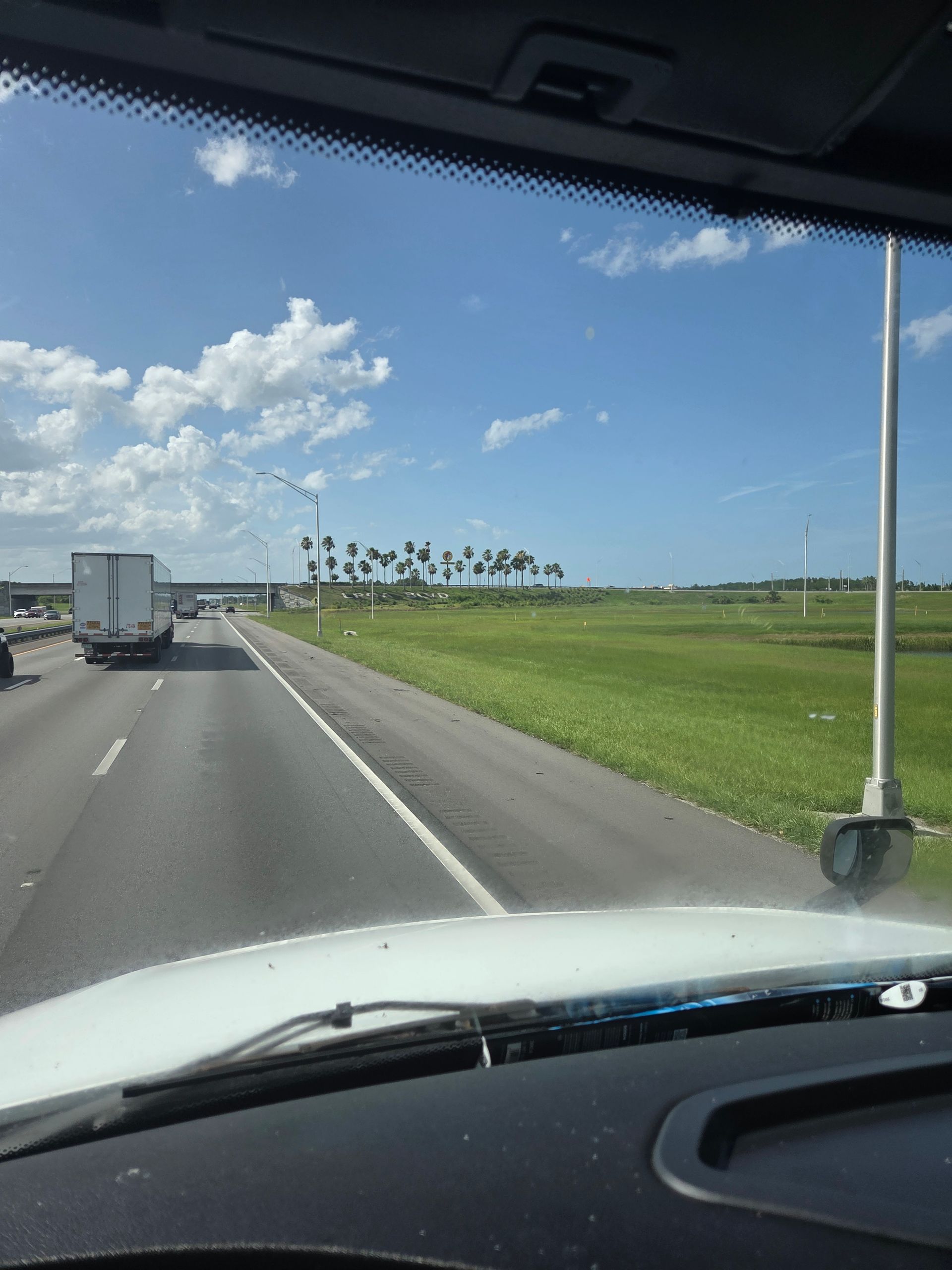 View from a car windshield on a highway with a truck, green field, and blue sky.