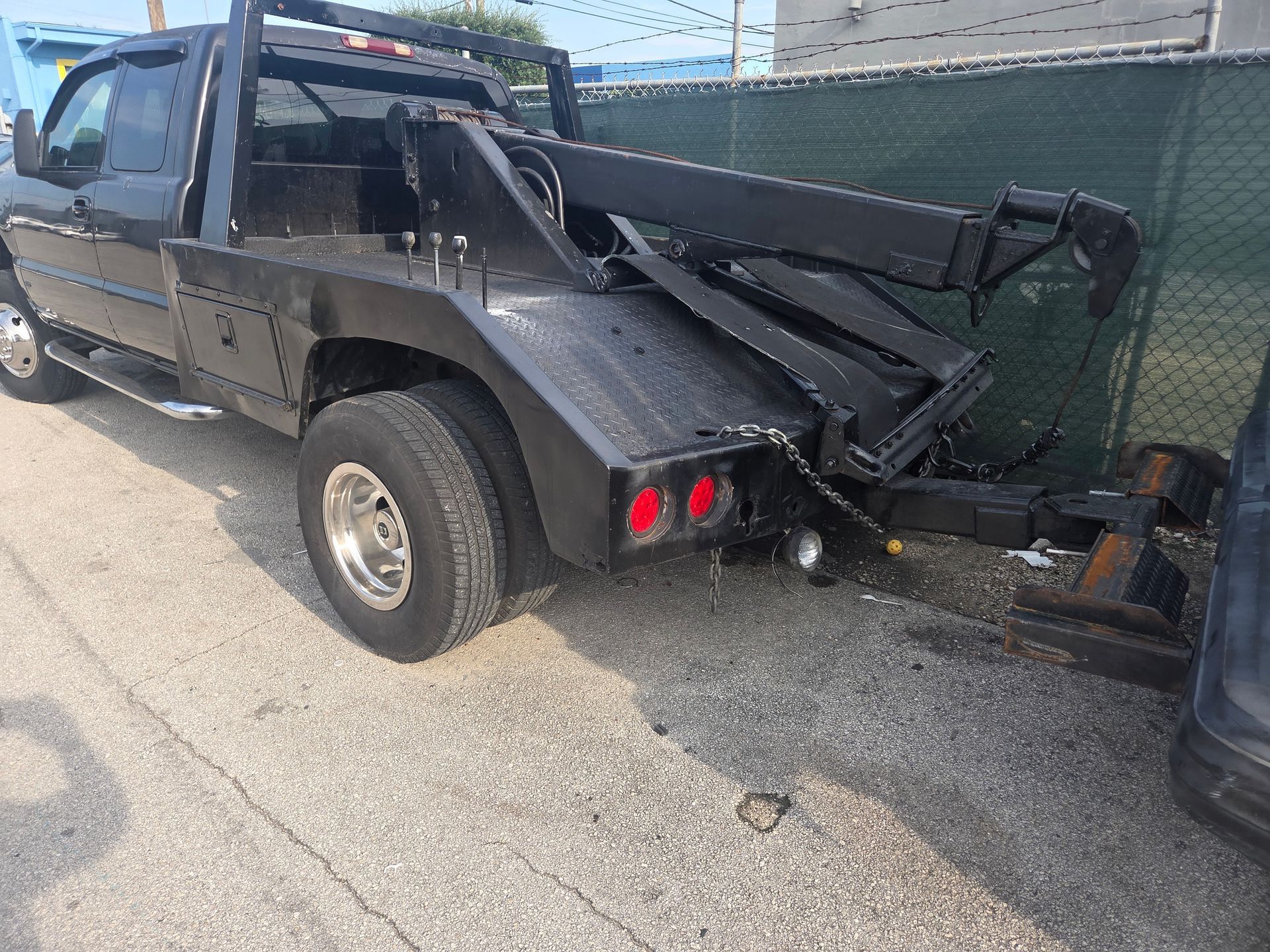 Black tow truck parked on gravel next to a chain-link fence.