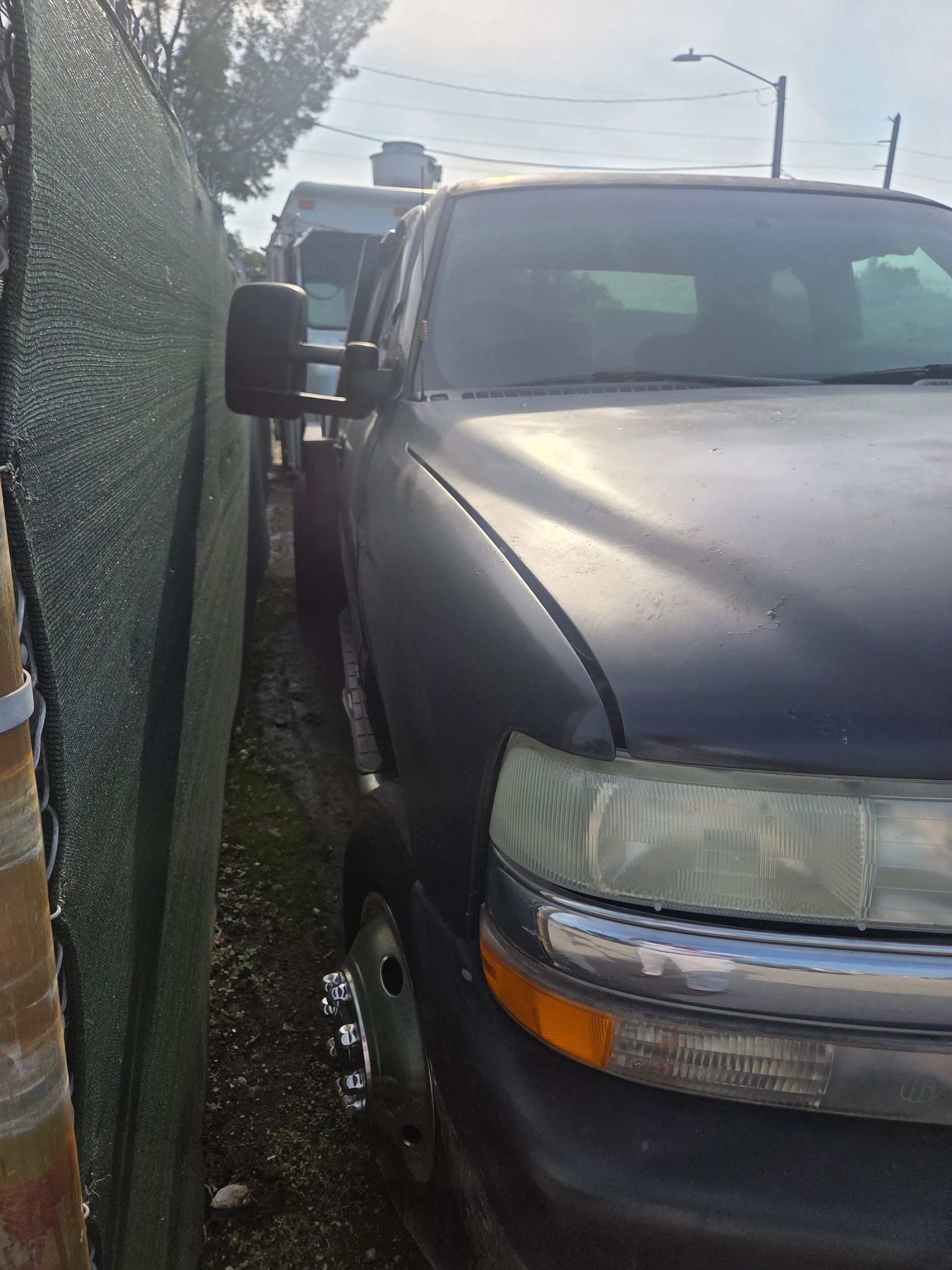Dark pickup truck parked next to a wall. Headlights and side mirror visible.