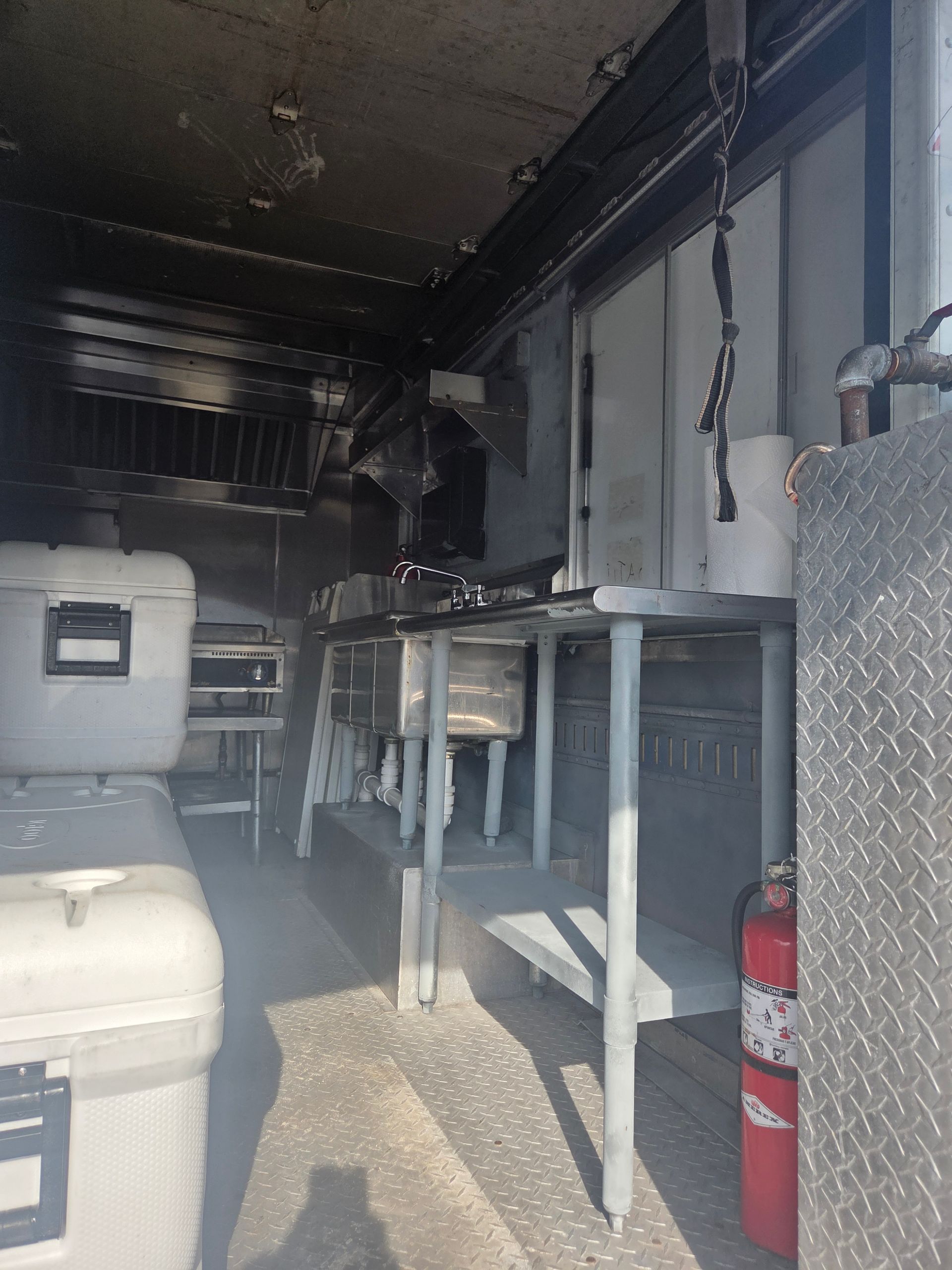 Interior of a food truck after a fire. Blackened areas on the ceiling, metal tables, and a fire extinguisher.