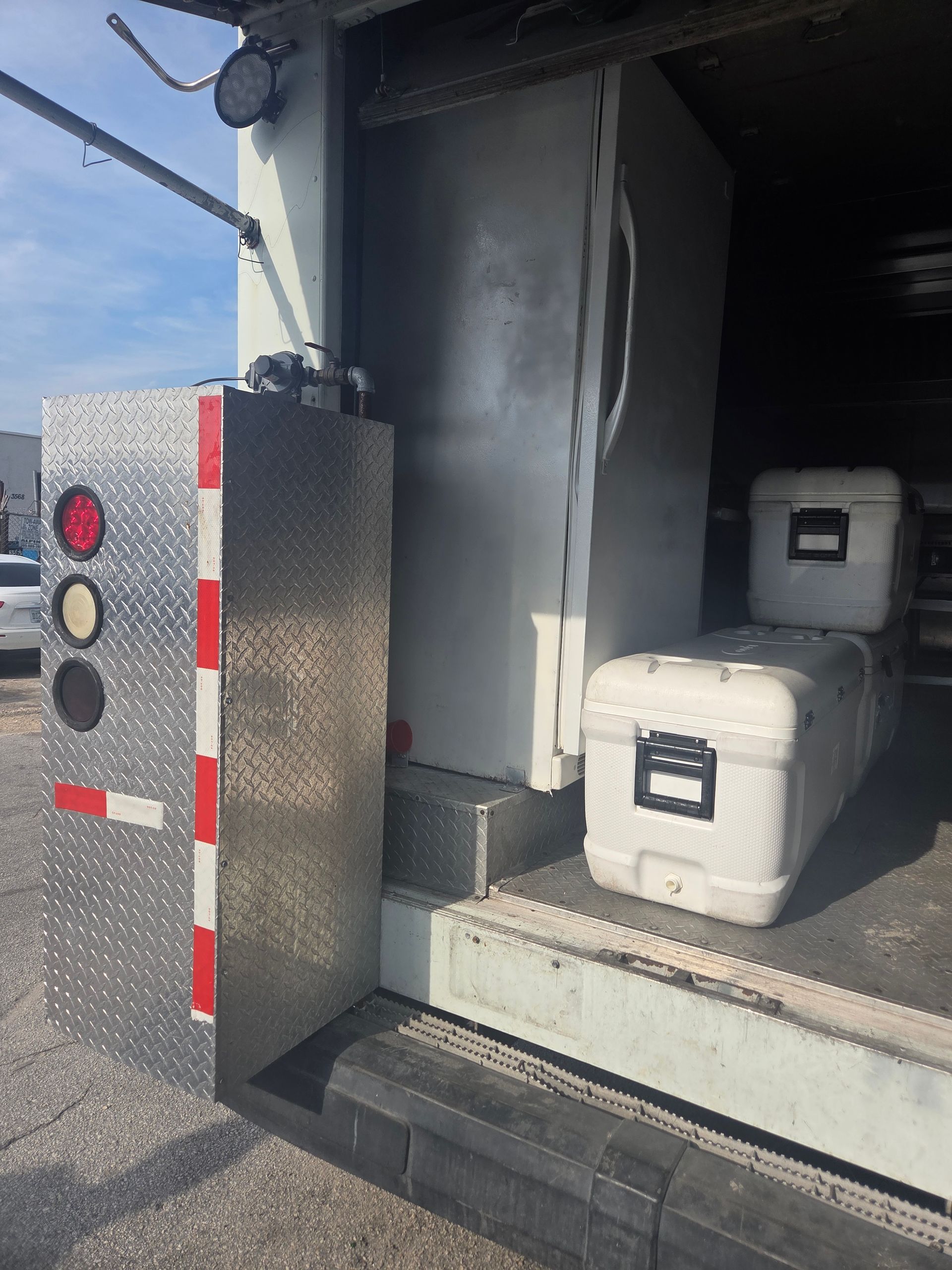 Truck's open door reveals a large refrigerator and two white containers on the loading platform; a signal panel is on the side.