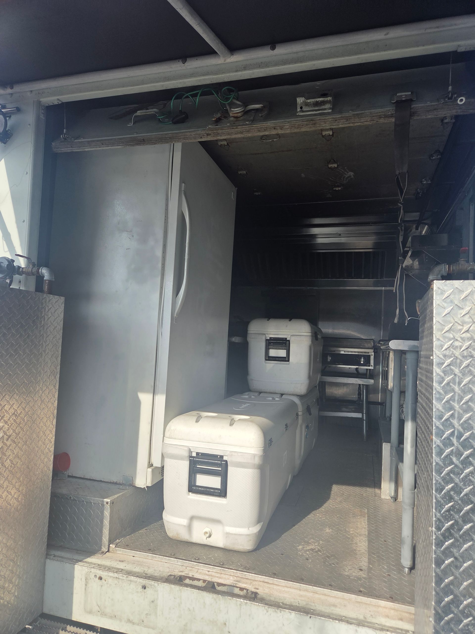Inside a truck: refrigerator, two white storage cases, and metal shelving.
