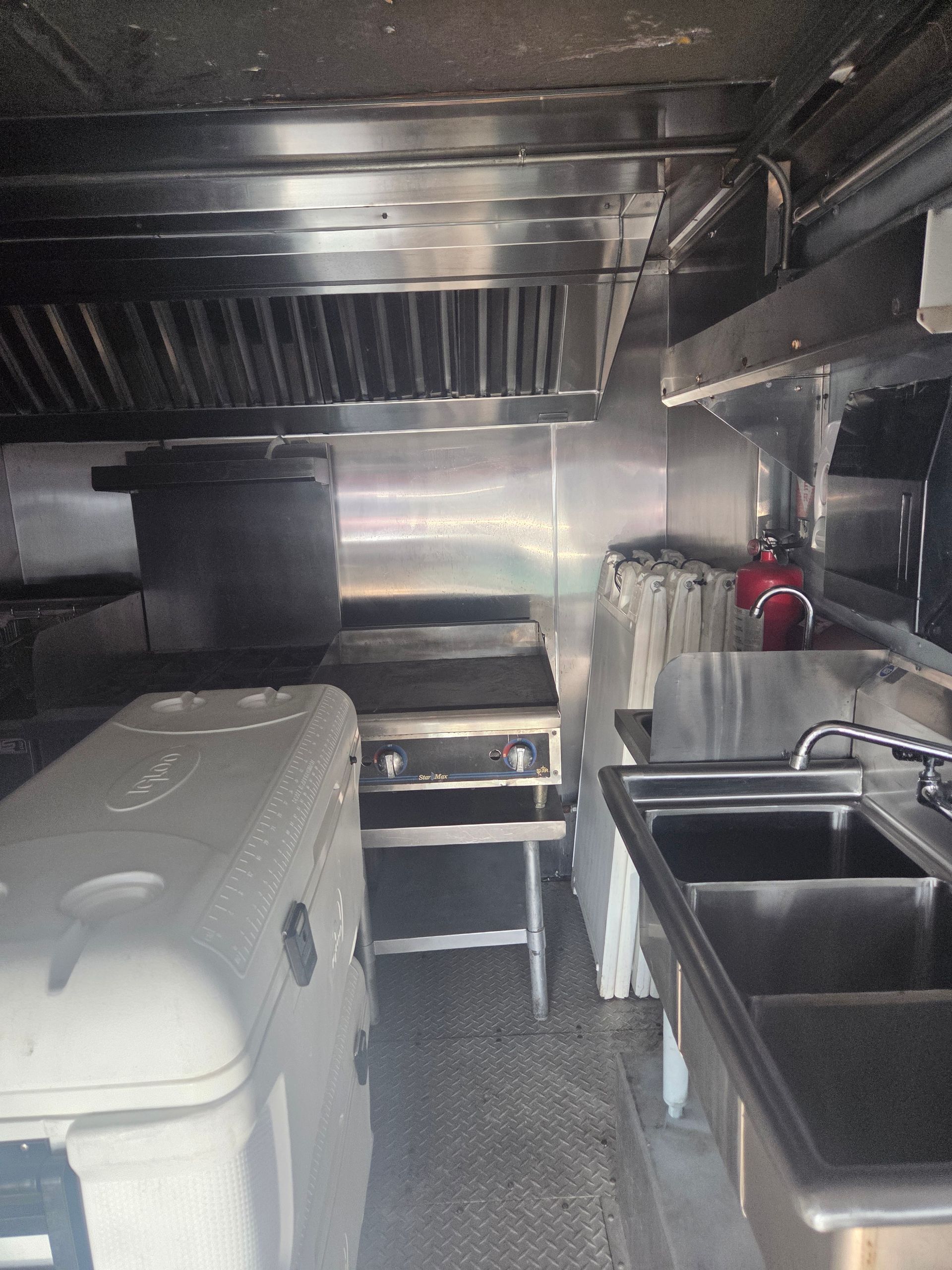Interior of a food truck. Stainless steel kitchen equipment includes a stove, sinks, and range hood.