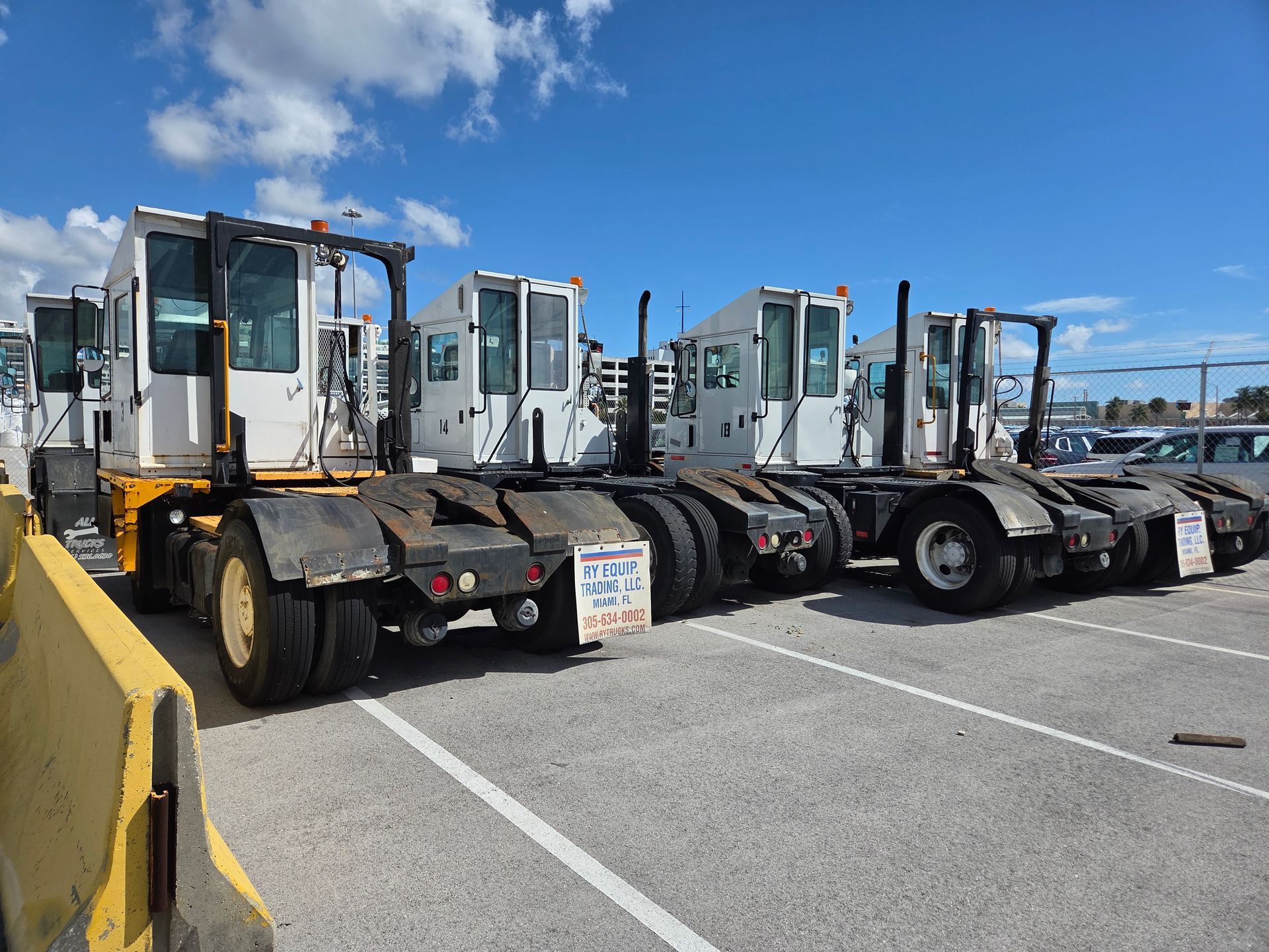 Three white and yellow terminal tractors parked on an asphalt lot under a blue sky.