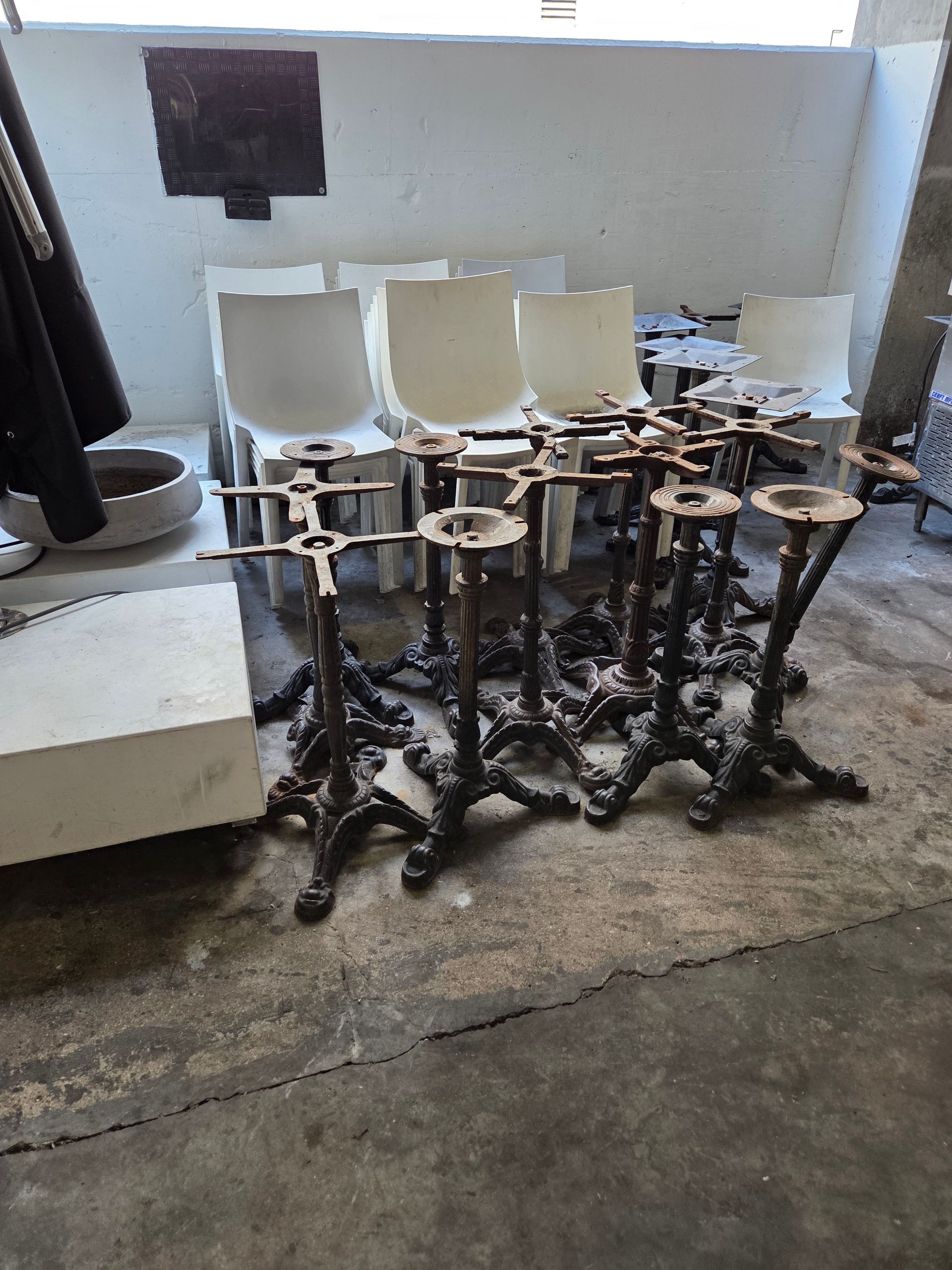 Metal table bases and white plastic chairs stacked indoors.