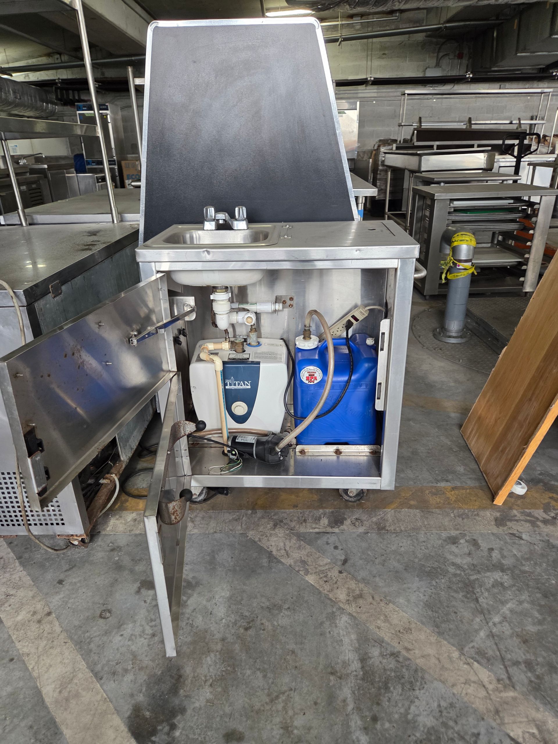Stainless steel machine with opened door, revealing internal components. A blue tank is visible. Industrial setting.