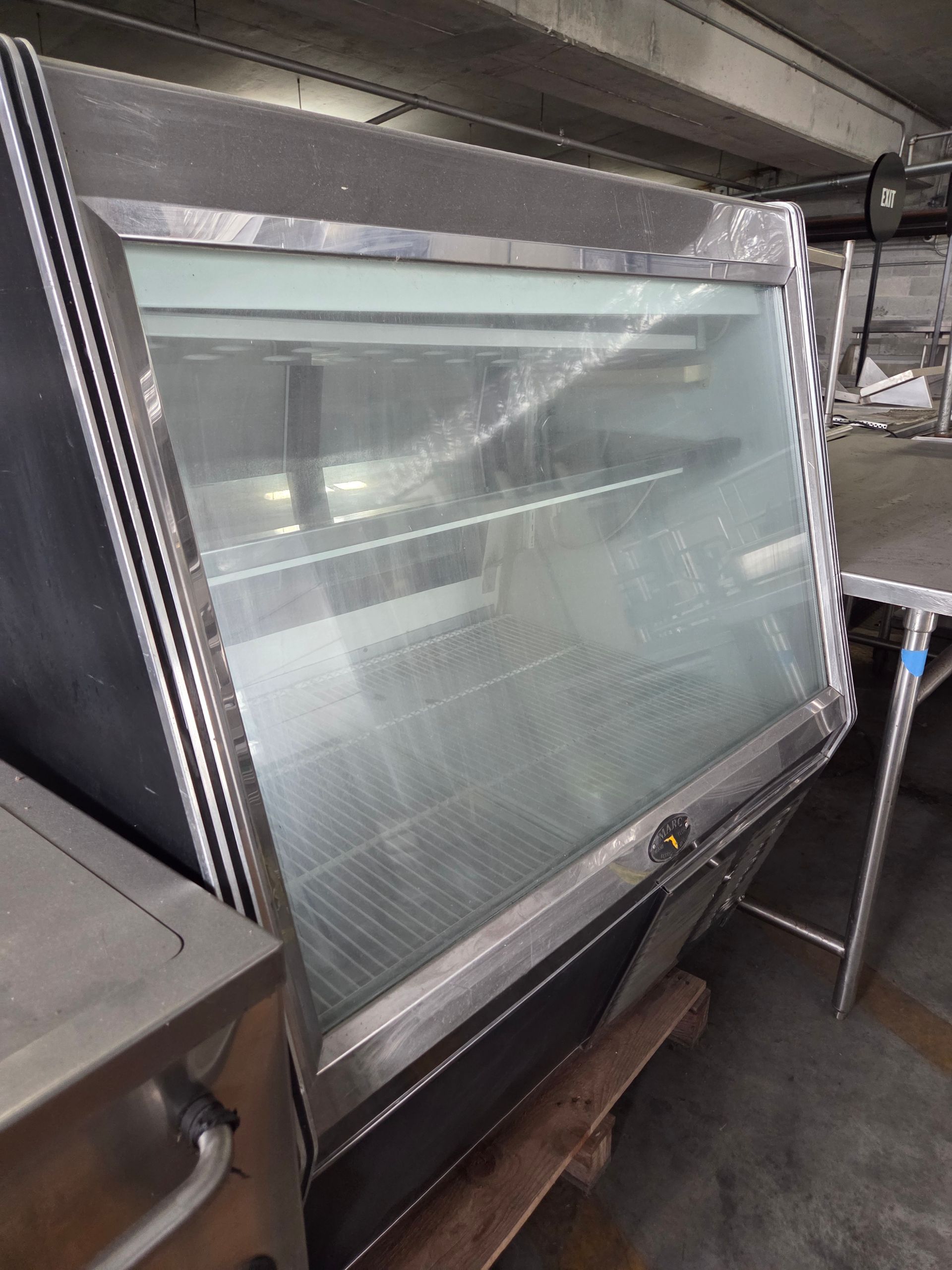 Stainless steel refrigerated display case with a glass front, in a commercial setting.