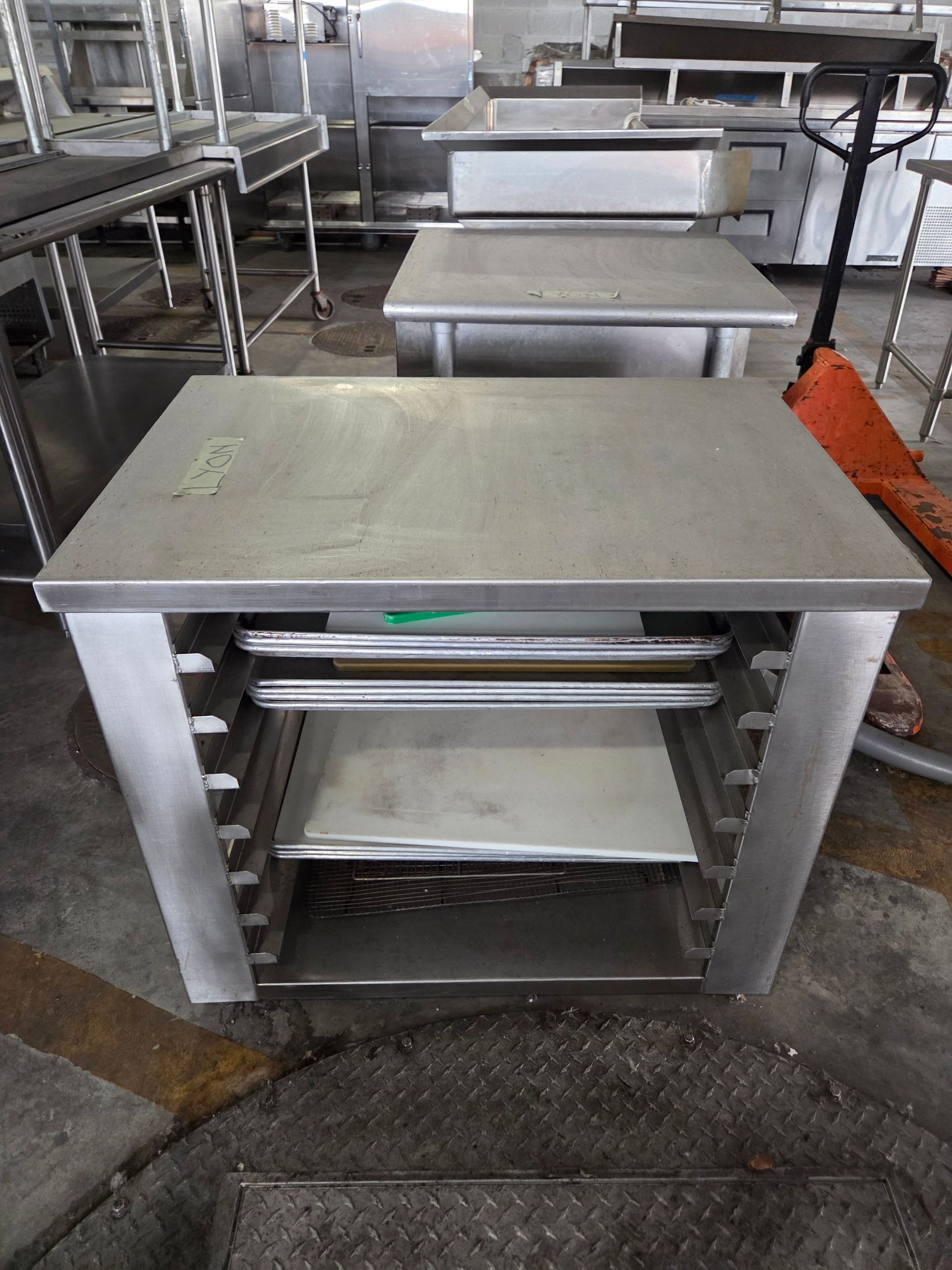 Stainless steel commercial kitchen work tables with open shelves for storage.
