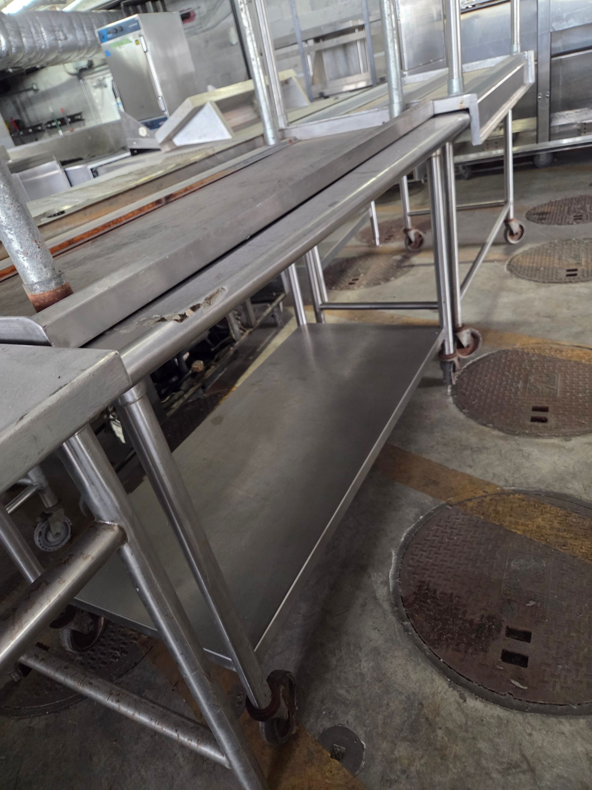 Stainless steel food preparation table on wheels in a commercial kitchen.